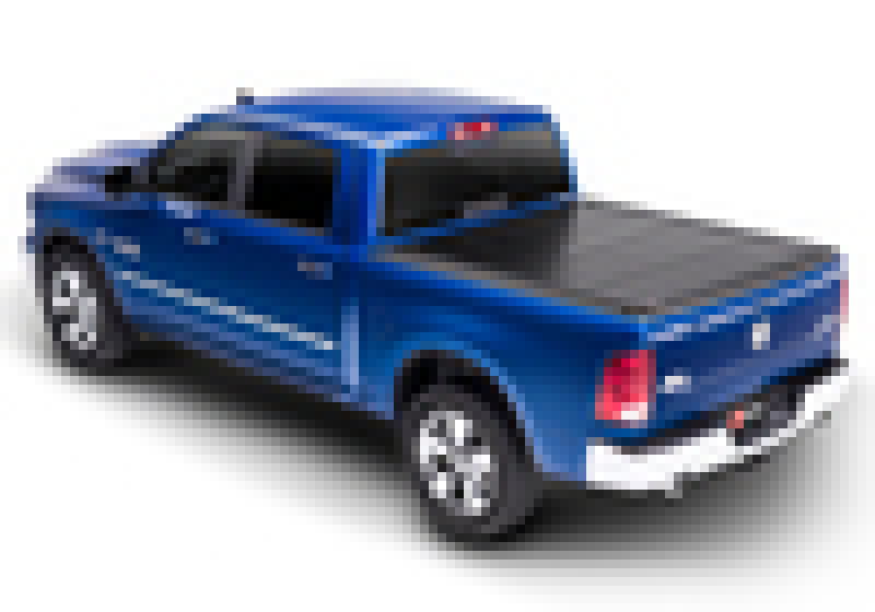 A blue pickup truck with a covered bed is shown in a three-quarter rear view. The vehicle has four doors, chrome wheels, and tinted windows. Its BAKFlip G2 hard folding truck bed cover from BAK provides full bed access and maximum theft protection for the 12-18 Ram 1500 (19-20 Classic Only) / 12-20 2500/3500 with a 6ft 4in bed.