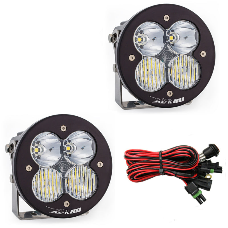 Two round Baja Designs XL R 80 Series LED light pods, each with three bulbs and a Driving Combo Pattern, are shown. They come in black housing with clear lenses, and include coiled red and black wiring with connectors. The brand "R80" is visible on the face of each light.