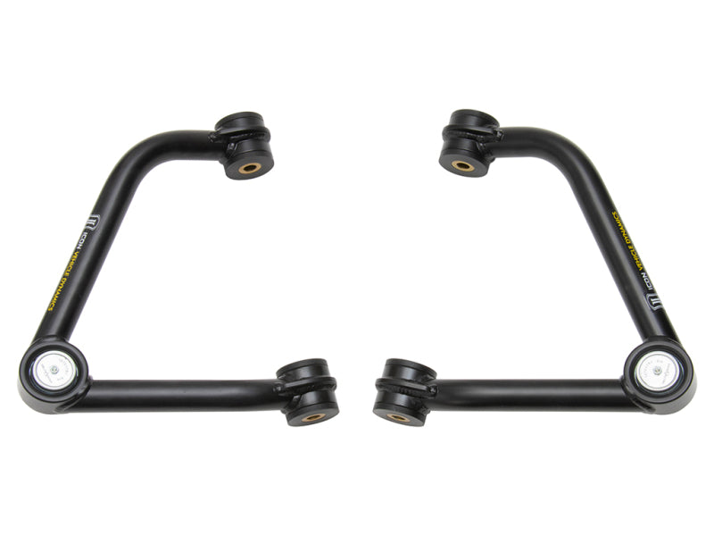 The image depicts the ICON 2019+ GM 1500 Tubular Upper Control Arm Delta Joint Kit, featuring a pair of black metal upper control arms for a vehicle's suspension system. Designed with multiple mounting points and bushings, each arm incorporates a heavy-duty high-angle Delta Joint. The control arms are symmetrically positioned and form an angled shape.