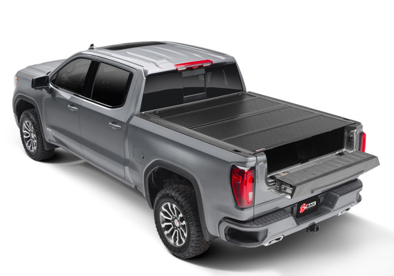 A BAK 2020 Chevy Silverado 2500/3500 HD with a 6ft 9in bed and a BAKFlip F1 hard folding truck bed cover is displayed from a rear three-quarter angle. The silver pickup truck, featuring a four-door cab, has its tailgate down to reveal an extended cargo storage drawer. The image is set against a plain white background.