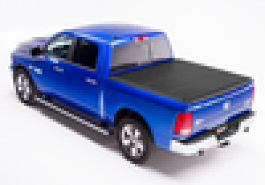 A Ram 1500 Classic pickup truck (09-18, 19-20 model) with a BAKFlip MX4 matte finish aluminum truck bed cover is viewed from the rear right side. The blue vehicle features chrome accents, including side steps and alloy wheels. Heavy-duty panels enhance its rugged appearance. The image is pixelated, obscuring finer details.