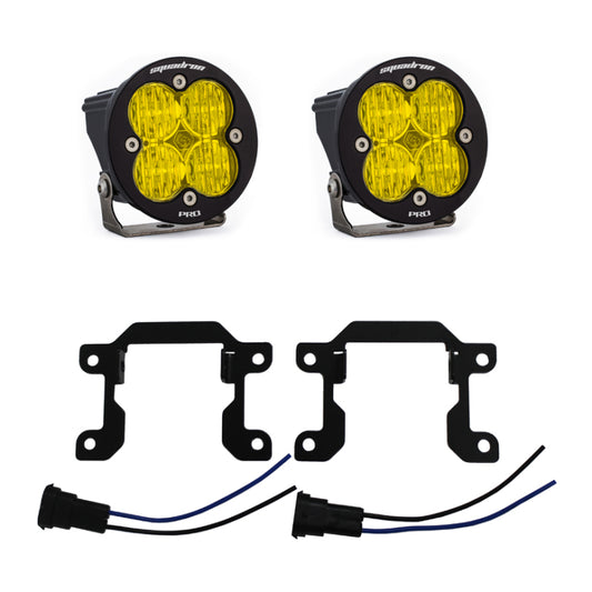 Two round, amber, four-LED pod lights from Baja Designs sit above black metal mounting brackets and two electrical connectors with blue and black wires. Branded as "Baja Designs," these rugged lights feature side-mounted brackets. Perfect for the 2019+ Ram 2500/3500 Big Horn Sports Fog Pocket Kit W/C - Amber, they add a striking visual enhancement.