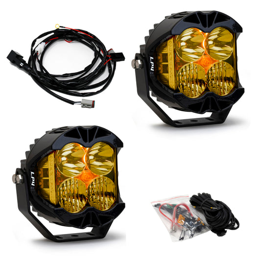 The Baja Designs LP4 Pro Driving/Combo LED - Amber (Pair) is displayed, featuring two yellow off-road LED lights with black housings. Adjacent to them is a wiring harness with connectors, and another set of wires and connectors is shown in a plastic bag. Their brilliant amber glow promises exceptional illumination in rugged terrains.