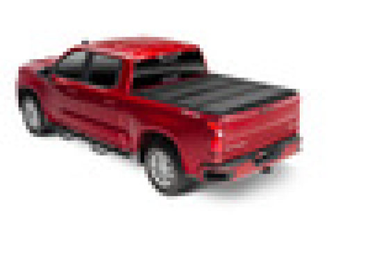 A red Chevy Silverado (New Body Style) with a 5ft 8in bed is shown from the rear three-quarter view, equipped with a BAKFlip MX4 Matte Finish heavy-duty truck bed cover by BAK. The truck has four doors, black side mirrors, and the bed cover features an aluminum matte finish. The pixelated image makes it difficult to discern finer details.