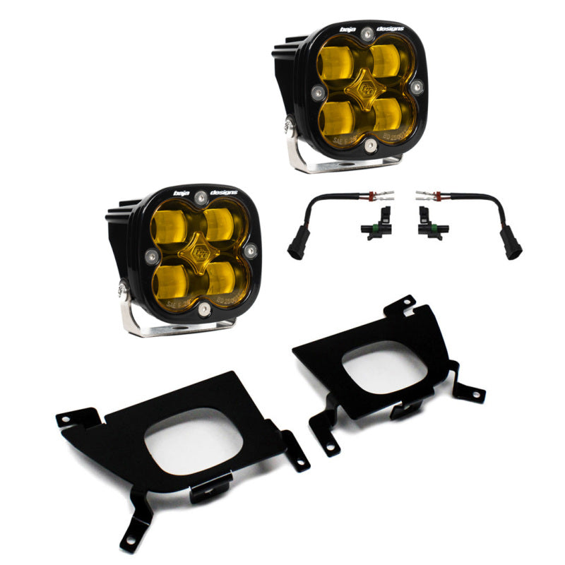 The image displays a Baja Designs 2019+ Chevy Silverado 1500/2500/2500 HD SAE Amber Fog Pocket Kit, featuring two amber square LED lights with black casings, two wiring harnesses, and two black metal mounting brackets. The components are arranged neatly on a white background.