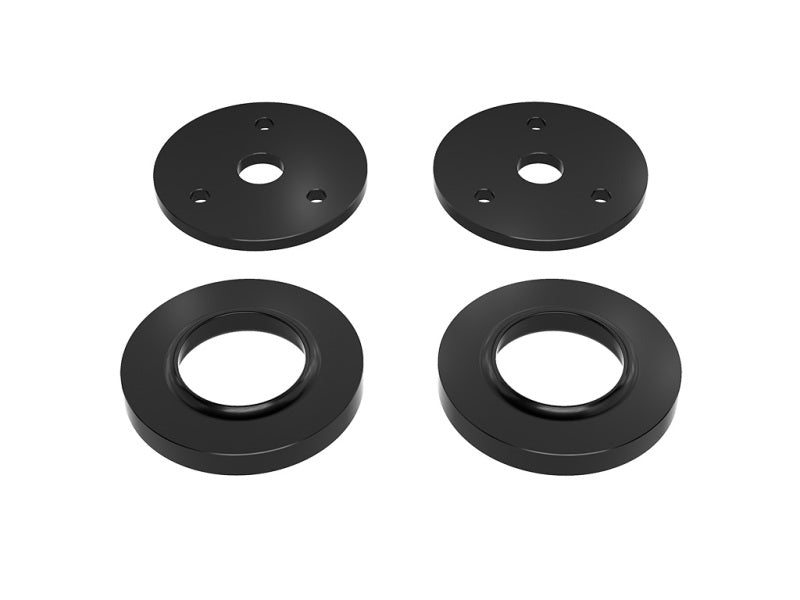 Four black metal washers, part of the ICON 2021+ Ram TRX 2in Lift Spacer Kit by ICON, are displayed against a white background. The top two feature three smaller holes and one larger central hole each, while the bottom two washers have a single circular hole in the center.