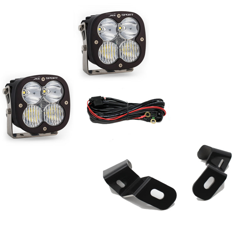 The Baja Designs 2019+ Ram 2500/3500 Sports Spot A-Pillar Kit includes two black square LED lights with four bulbs each, a wiring harness with red and black wires, and a pair of metal mounting brackets.