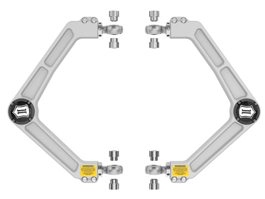 A symmetrical arrangement showcases two robotic arm mechanisms, constructed from corrosion-resistant grey material and adorned with black and yellow warning labels near the central Delta Joint. This pairs perfectly with the ICON 2019+ Ram 1500 Billet Upper Control Arm Delta Joint Kit by ICON, set against a plain white background.